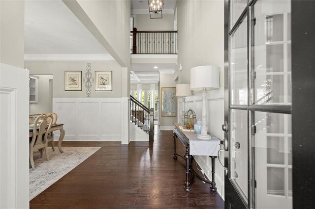 foyer entrance with wainscoting, a decorative wall, wood finished floors, ornamental molding, and stairway