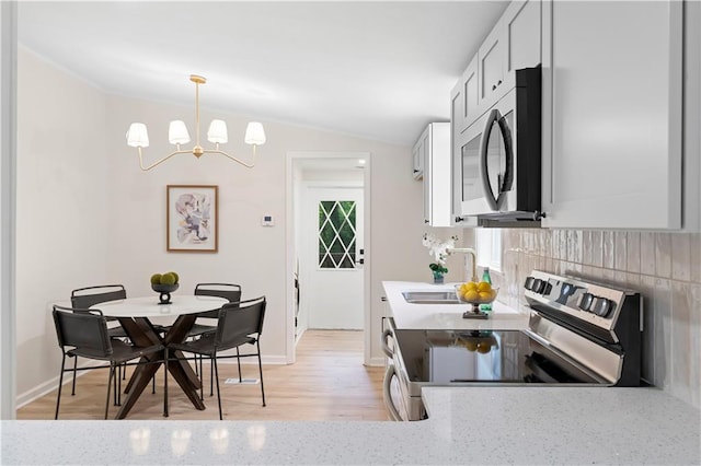 1010 Martin Ln, Canton, GA 30114 - kitchen featuring appliances with stainless steel finishes, a chandelier, lofted ceiling, light stone counters, and decorative backsplash