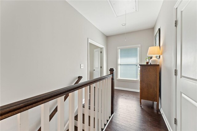 corridor featuring attic access, dark wood finished floors, baseboards, and an upstairs landing
