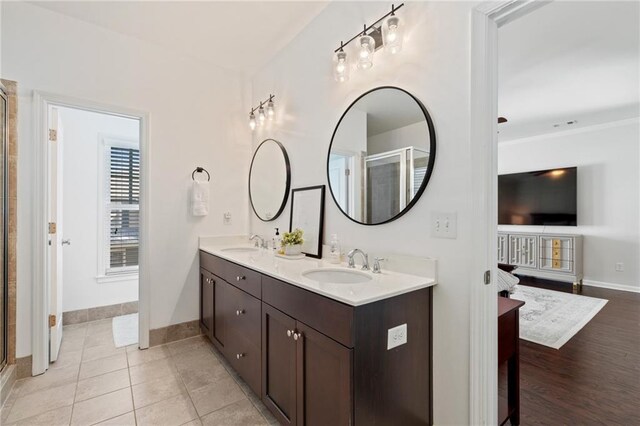 bathroom featuring baseboards, a shower stall, double vanity, and tile patterned flooring