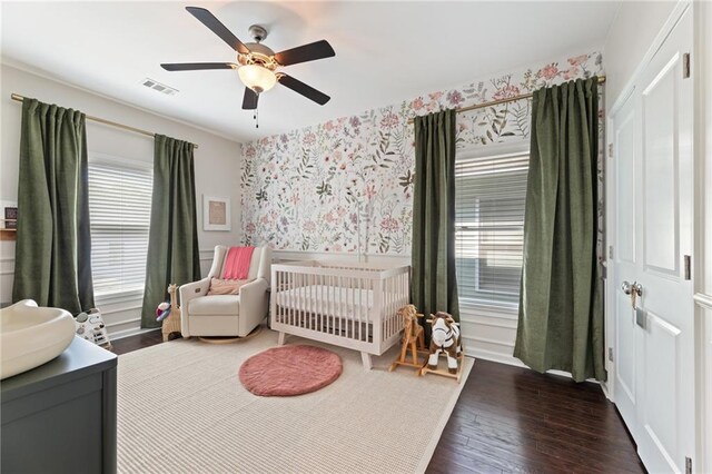 bedroom featuring a nursery area, wallpapered walls, wood finished floors, ceiling fan, and a closet