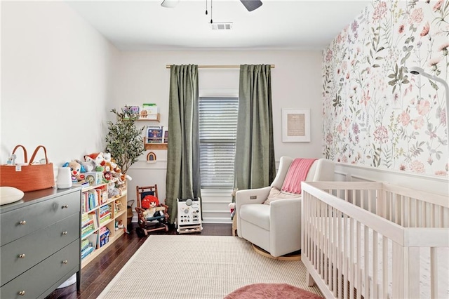 bedroom featuring a crib, wood finished floors, and ceiling fan