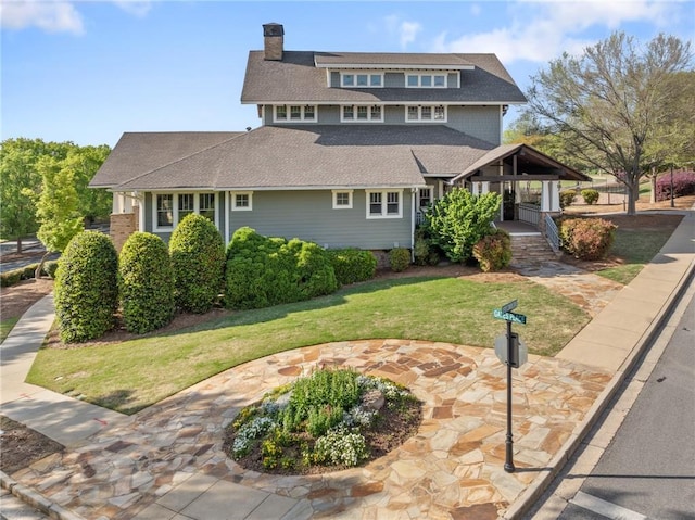 view of front of house featuring a chimney, a front lawn, covered porch, and a shingled roof