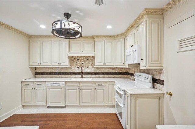 kitchen with backsplash, sink, pendant lighting, light wood-type flooring, and white appliances