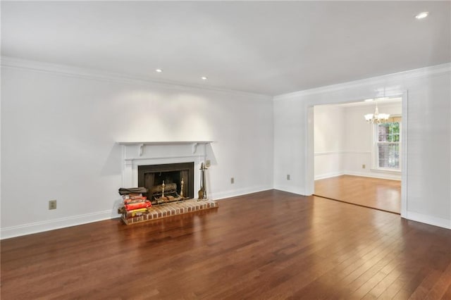 unfurnished living room with a brick fireplace, ornamental molding, a chandelier, and dark hardwood / wood-style flooring