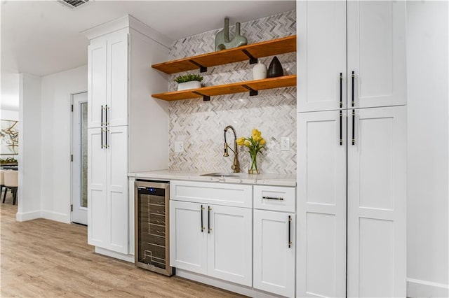 bar with a sink, decorative backsplash, light wood finished floors, baseboards, and wine cooler