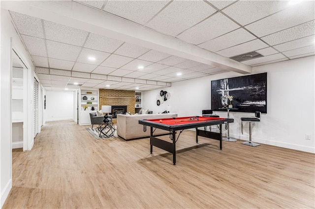 playroom with baseboards, a brick fireplace, wood finished floors, and a paneled ceiling