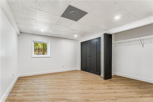 unfurnished bedroom featuring two closets, light wood finished floors, baseboards, and a drop ceiling