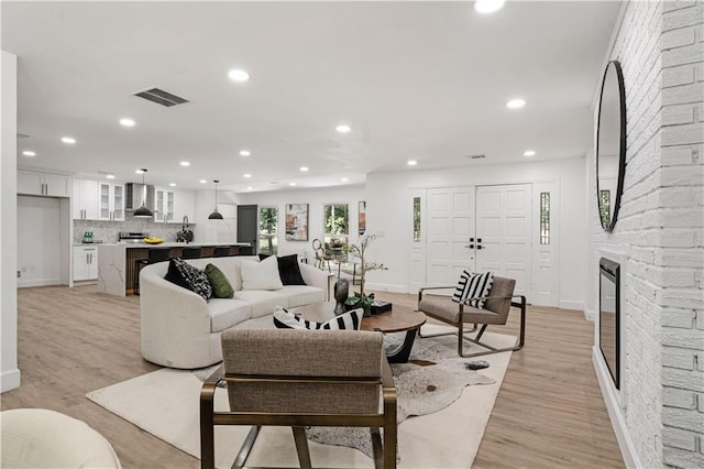 living room with recessed lighting, light wood-style flooring, visible vents, and a large fireplace