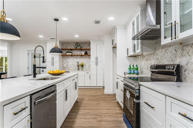 kitchen with stainless steel appliances, a sink, visible vents, decorative backsplash, and wall chimney range hood