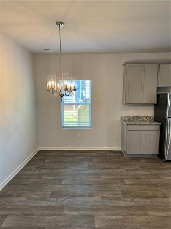 unfurnished dining area featuring dark wood-type flooring and an inviting chandelier