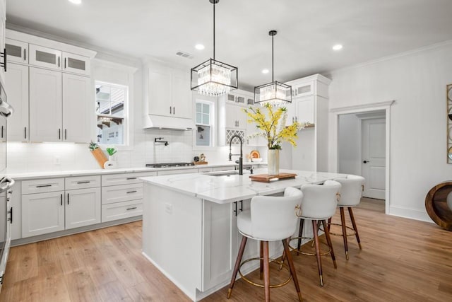 kitchen featuring white cabinetry, stainless steel gas cooktop, a sink, light wood finished floors, and light stone countertops