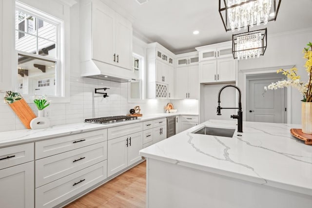 kitchen featuring white cabinetry, under cabinet range hood, a sink, stainless steel gas stovetop, and glass insert cabinets