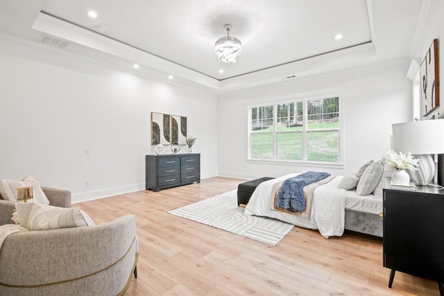 bedroom with light wood-style flooring, a tray ceiling, and visible vents