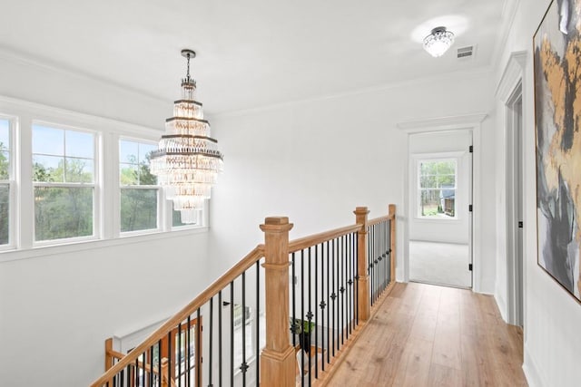 hallway with an upstairs landing, crown molding, a chandelier, visible vents, and wood finished floors