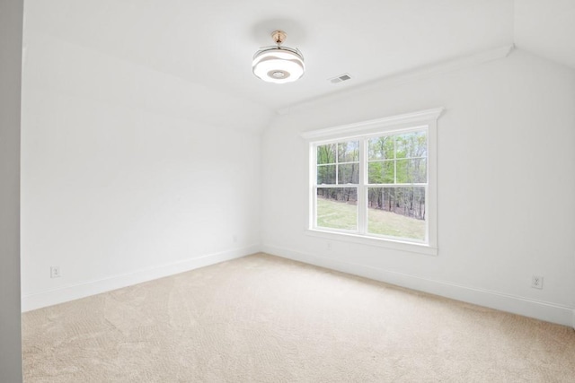 spare room with baseboards, lofted ceiling, visible vents, and light carpet