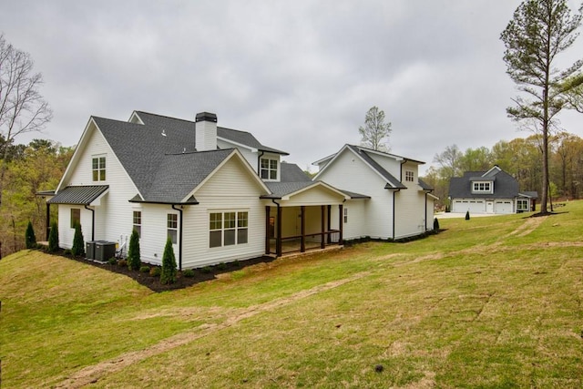 rear view of property with central air condition unit, a lawn, a chimney, and a shingled roof