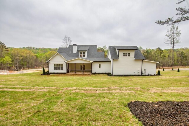 back of house featuring a lawn and a wooded view