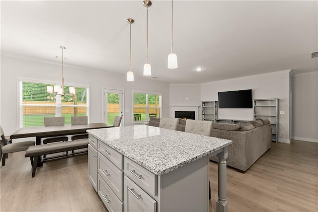 kitchen featuring a center island, light wood-style flooring, crown molding, hanging light fixtures, and gray cabinets