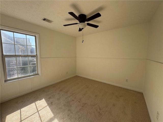 spare room featuring baseboards, visible vents, a ceiling fan, light colored carpet, and a textured ceiling