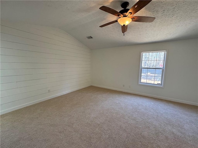 carpeted empty room featuring lofted ceiling, visible vents, a textured ceiling, and baseboards