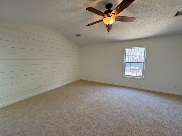 carpeted spare room with vaulted ceiling, a textured ceiling, visible vents, and baseboards