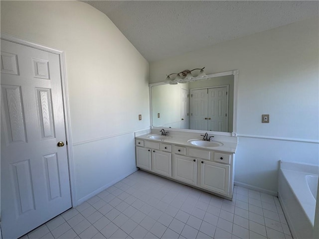 bathroom featuring double vanity, a textured ceiling, vaulted ceiling, and a sink