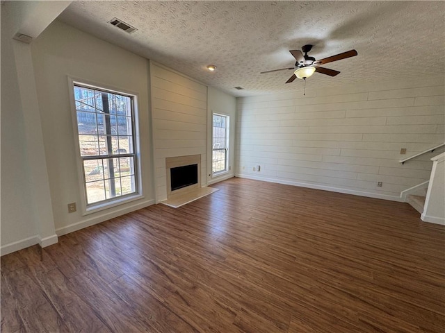 unfurnished living room with ceiling fan, a large fireplace, dark wood-type flooring, visible vents, and baseboards