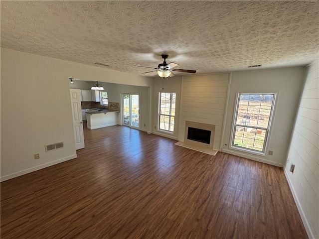 unfurnished living room with dark wood-type flooring, a large fireplace, visible vents, and ceiling fan