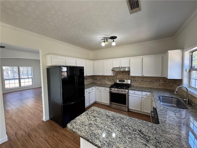 kitchen featuring freestanding refrigerator, white cabinets, stainless steel gas stove, a sink, and under cabinet range hood