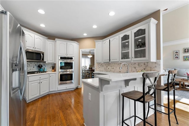 1254 Hadaway Garden Dr NW, Kennesaw, GA 30152 - kitchen featuring stainless steel appliances, a peninsula, a kitchen bar, glass insert cabinets, and dark wood finished floors