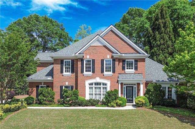 colonial house with roof with shingles, brick siding, and a front lawn