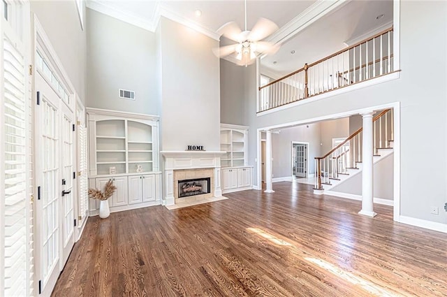 unfurnished living room with baseboards, a tiled fireplace, ceiling fan, crown molding, and a towering ceiling