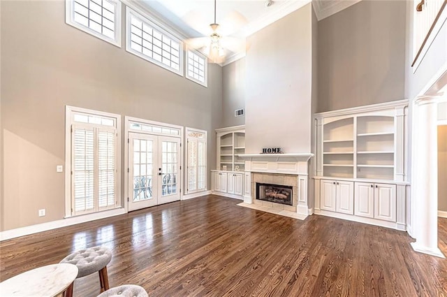 unfurnished living room with a ceiling fan, a high ceiling, a tiled fireplace, ornamental molding, and dark wood-style floors