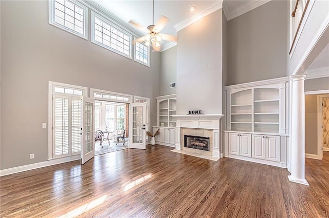 unfurnished living room featuring a ceiling fan, baseboards, crown molding, a towering ceiling, and wood finished floors