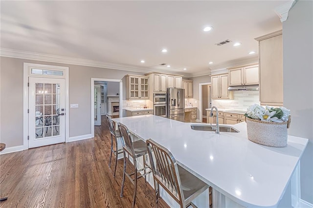 kitchen with a sink, a peninsula, crown molding, stainless steel appliances, and cream cabinets