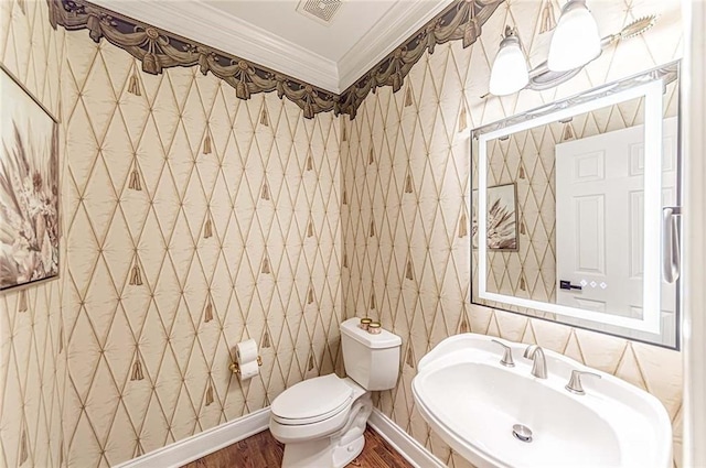 half bath with toilet, wood finished floors, a sink, crown molding, and visible vents