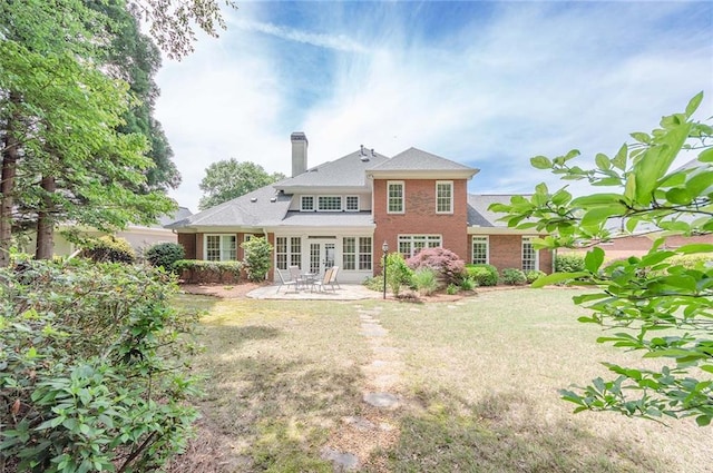 back of house with a yard, a patio area, a chimney, and brick siding