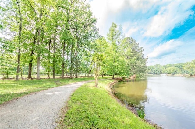 surrounding community featuring a water view, a wooded view, and a lawn