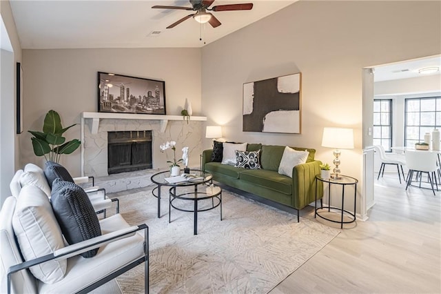 living room featuring ceiling fan, lofted ceiling, a stone fireplace, and light hardwood / wood-style floors