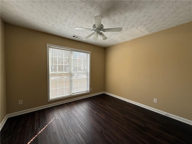 empty room with dark wood-style floors, a ceiling fan, visible vents, and baseboards