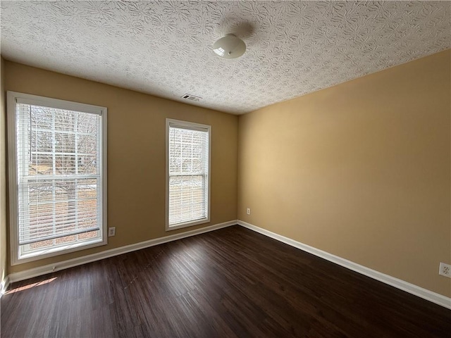 unfurnished room featuring visible vents, baseboards, dark wood finished floors, and a textured ceiling