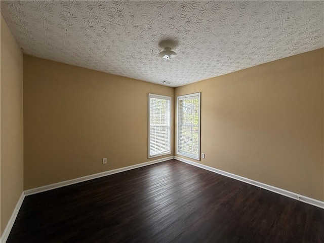 empty room with dark wood-style floors, visible vents, a textured ceiling, and baseboards