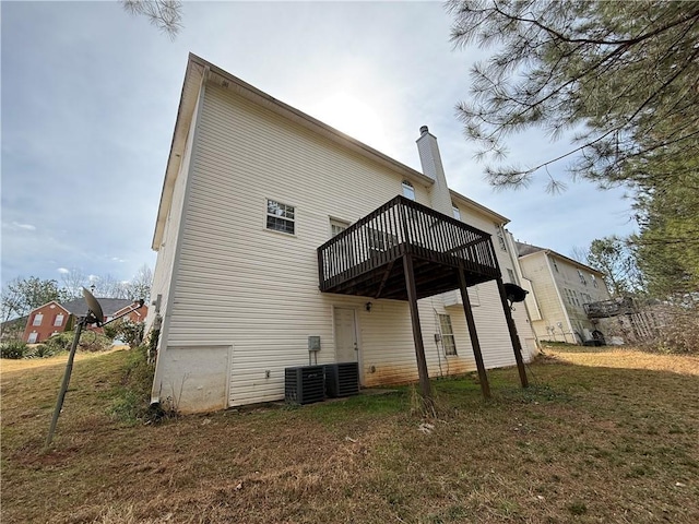 rear view of property with a deck, central AC unit, a lawn, and a chimney