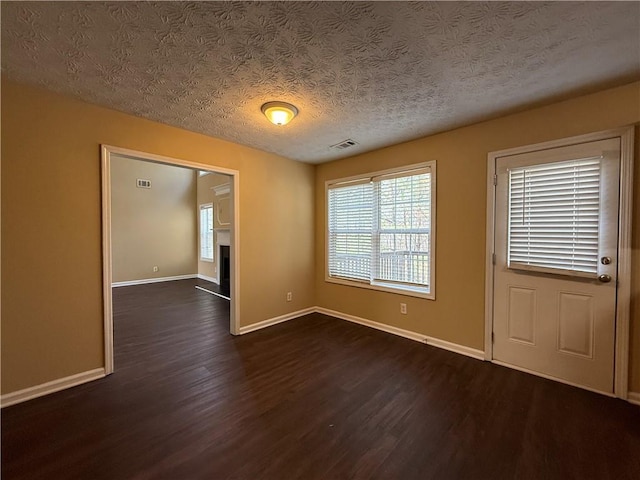 interior space with a fireplace with raised hearth, a textured ceiling, dark wood-type flooring, visible vents, and baseboards