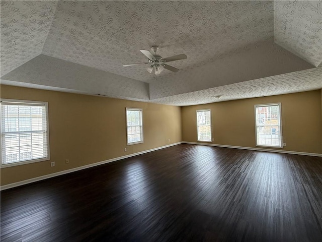 spare room featuring a textured ceiling, wood finished floors, a raised ceiling, and baseboards