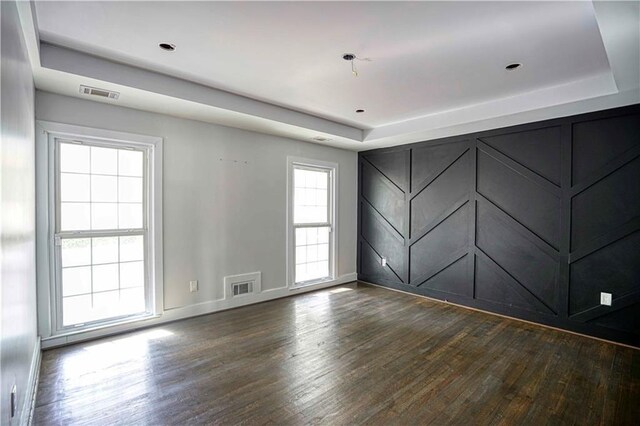 empty room with dark hardwood / wood-style flooring and a raised ceiling