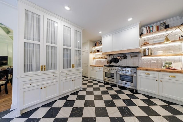 kitchen featuring double oven range, butcher block counters, decorative backsplash, white cabinets, and open shelves