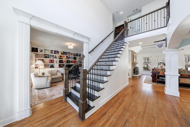 stairway with wood finished floors, baseboards, a high ceiling, decorative columns, and a stone fireplace