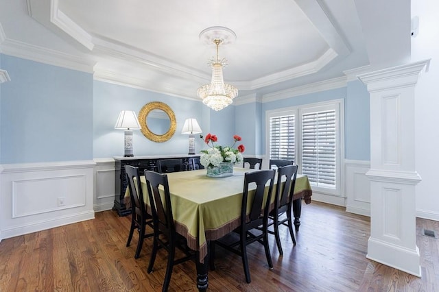 dining room featuring dark wood finished floors, a tray ceiling, decorative columns, wainscoting, and a chandelier